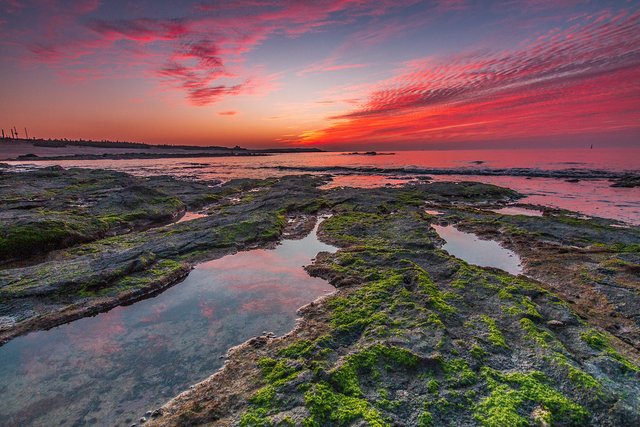 Crimson dusk sky over rock pools at the shore